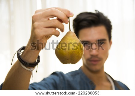 Young man holding a large delicious ripe yellow pear dangling from his hand, focus to the pear