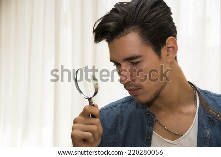 Young man looking through a magnifying glass in a conceptual image of a detective searching for clues, inspection, examination or analysis