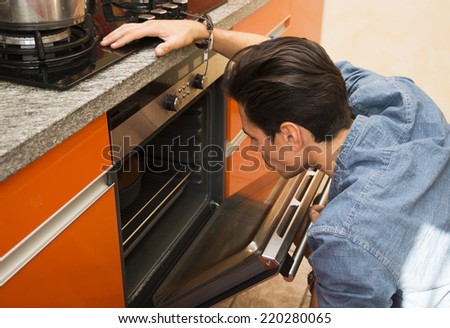 Man watching something cook in the oven in his orange kitchen bending down to look inside the stove to check if it is ready