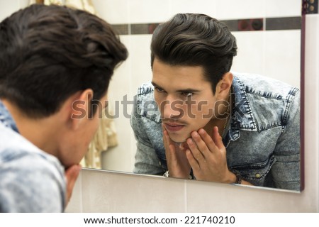 Close Up of Young Man Examining Face in Reflection of Mirror and Glaring at Self