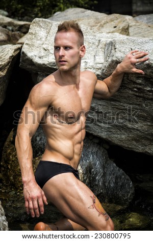 Handsome young muscle man standing in water pond, naked wearing only swimming suit