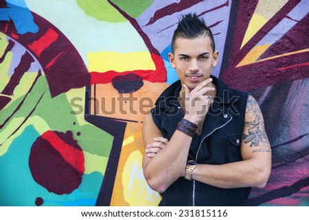 Handsome young man standing against graffiti covered wall looking at camera smiling