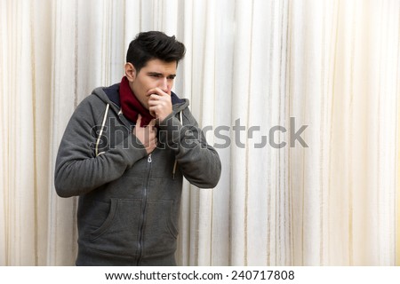 Sick young man with flu or cold, coughing with hand on his mouth. Indoor shot at home