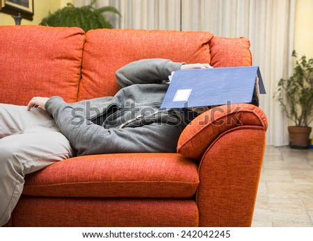 Over-worked, tired young man at home sleeping instead of working or studying, resting with head covered by book