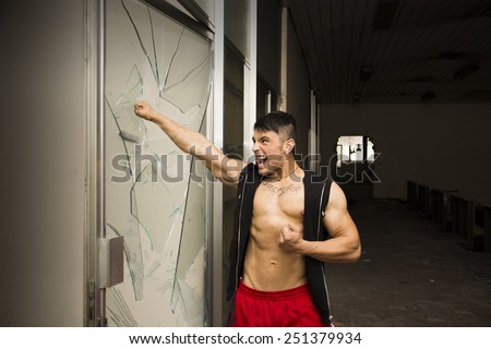 Violent muscular young man, a vandal breaking door glass in abandoned building
