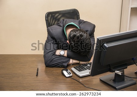 Overworked, tired young businessman sleeping on his desk  in office, in front of computer