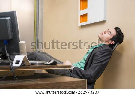 Overworked, tired young businessman sleeping at his desk  in office, in front of computer