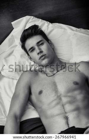 Handsome shirtless athletic young man laying in bed at night looking at camera, seen from above