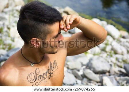 Attractive muscular shirtless young man in nature shielding eyes from sun with his hand