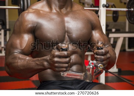 Hunky muscular black bodybuilder working out in gym, exercising back on machine