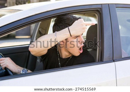 Handsome Young Man Driving a Car and showing the middle finger to someone behind him