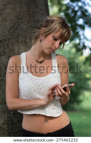 Attractive blonde young woman outdoors using cell phone, typing and sending messages