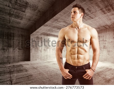 Muscular shirtless young man with jeans, indoors in empty warehouse. Looking to a side
