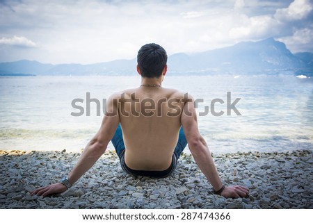 Muscular shirtless young man\'s back, sitting on a lake in a sunny, peaceful day, sitting on a wood pier, thinking or meditating
