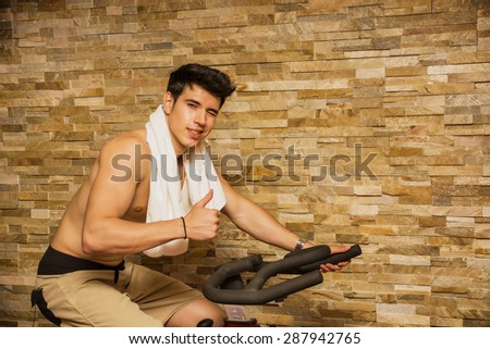 Attractive young man exercising in gym: spinning on stationary bike