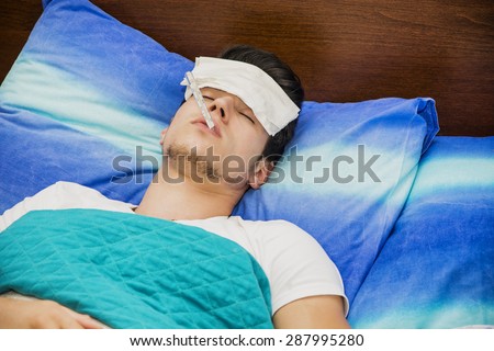 Young handsome man in bed with a flu or measuring fever with thermometer in his mouth