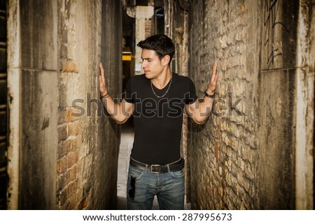 Young man pressed between two walls. Concept of oppression, anxiety. Standing in Narrow Hallway of Decrepit Abandoned Brick Industrial Building