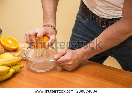 Young man squeezing an orange to prepare healthy fruit salad or smoothie on a kitchen counter loaded with an assortment of fresh fruit