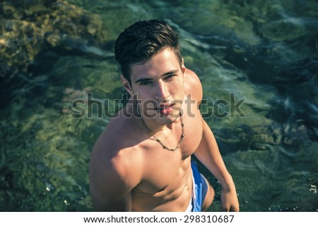 Muscular handsome young man at sea seen from above perspective, looking at camera