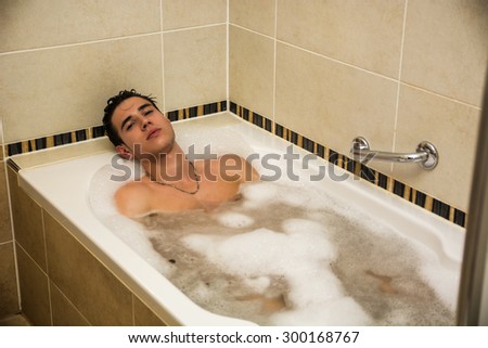 Handsome young man in bathtub at home having bath, looking at camera