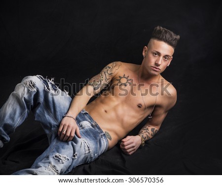 Young hip man in jeans, shirtless, isolated on black background in studio shot