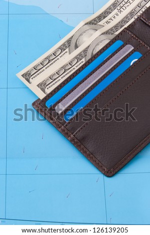 Wallet with dollars cash and credit cards on map background for travel concept.