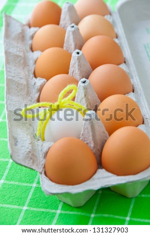 One white egg  in a carton package of brown eggs. selective focus