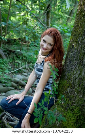 Pretty redhead woman in camouflage shirt, sitting against a tree trunk