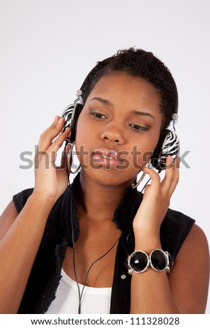 Pretty black woman listening to music with earphones around her neck and looking down with a pleased expression