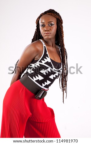 Pretty black woman with long dread locks and wearing red pants, looking at the camera with a thoughtful and quiet expression while leaning forward