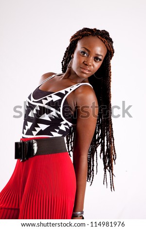 Pretty black woman with long dread locks and wearing red pants, looking at the camera with a thoughtful and serious expression