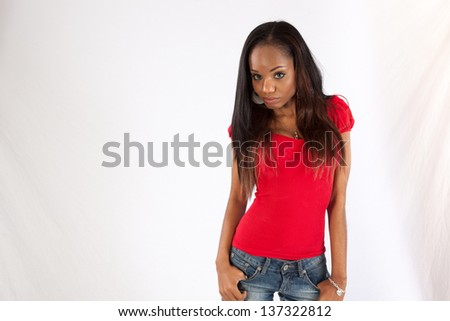 Lovely black woman in red blouse, blue jean cut offs, and long hair, looking at the camera with a thoughtful, serious, but  friendly expression