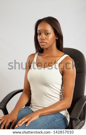 Lovely black woman in a white, tank top, sitting in a executive chair, and looking left with a calm, but serious, pensive  expression