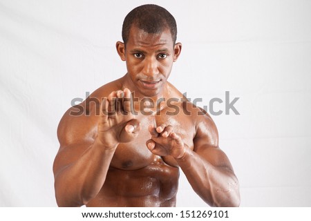 Muscular black man shirtless with his chest, abdomen and arms glistening with sweat,  in a marshal arts stance of ready