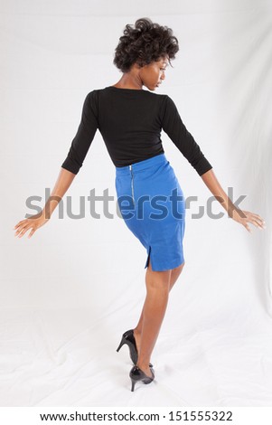 Pretty black woman in black blouse and blue dress, with her back to the camera and  a serious, thoughtful expression
