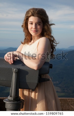 Pretty Caucasian woman standing with a viewer at a mountain overlook and looking at the camera with a friendly, happy, smile