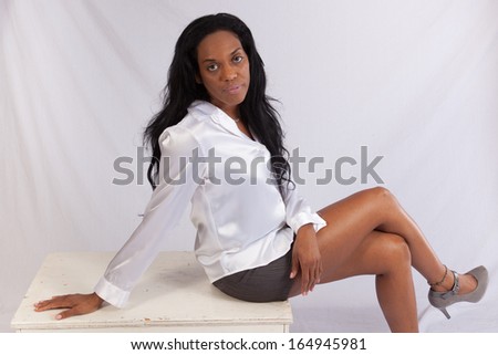 Lovely black woman in a white, silk blouse,  sitting and looking at the camera with a pleasing expression