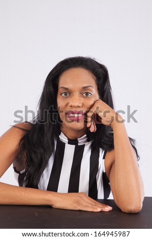 Lovely black woman in a white, silk blouse,  sitting and looking at the camera with a pleasing expression