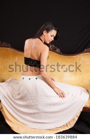 Pretty woman in black top and dress sitting  on a gold couch with her back to the camera