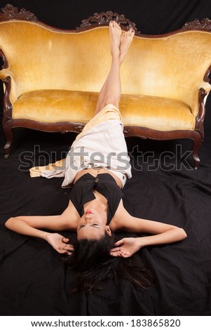 Pretty Caucasian woman laying down with  a gold couch and  with a serious but friendly expression
