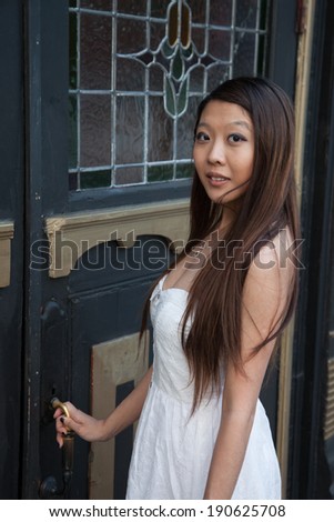 East Asian woman, outside opening a door, with eye contact and a friendly, pleased smile for the camera