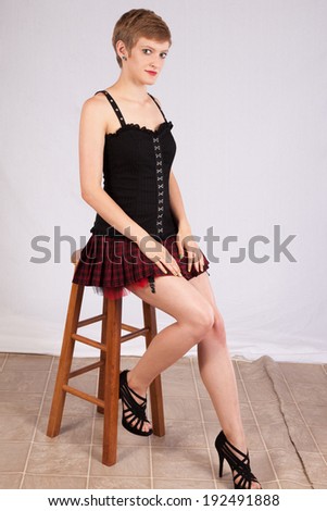 Pretty short haired, Caucasian woman sitting on a wooden stool, with a friendly look for the camera