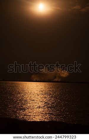 Rocket being launched into outer space at night, and reflecting on water