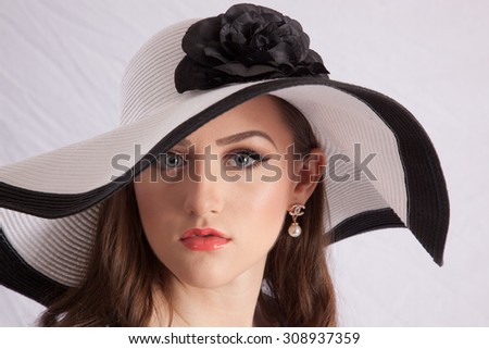 Pretty Caucasian woman in white hat with black rim and bow, looking thoughtfully