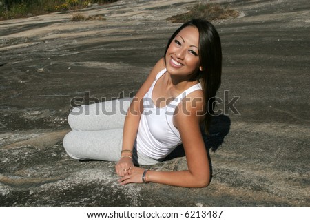 Asian woman laying down on a rock in the sunshine