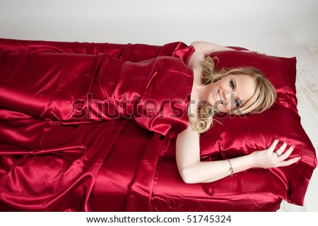 Beautiful blond woman in bed with red satin sheets