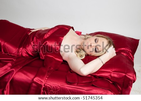 Beautiful blond woman in bed with red satin sheets