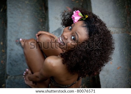 Lovely black woman outside in a swimsuit with pink flower in her hair and a friendly smile on her face