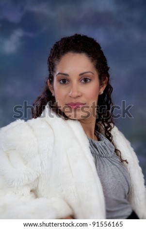 Pretty caucasian woman In a white fur coat looking at the camera and leaning gently on her right arm.