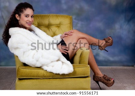 Pretty caucasian woman sitting sideways in a chair with her legs over the armrest and  a  big smile and eye coatact